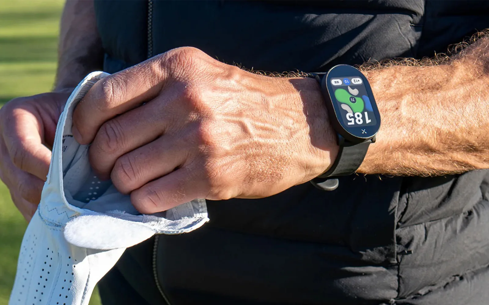 Golfer pulling on a glove while wearing the PlayMaker+ smartwatch on the course