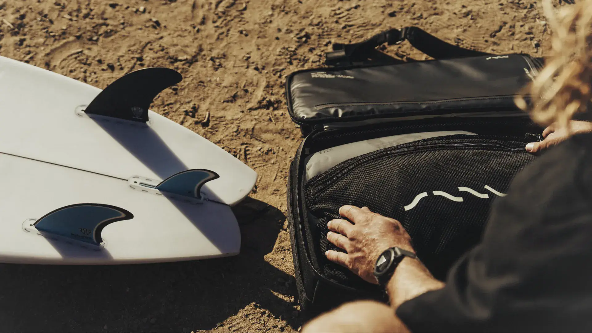 Surfer opening the SAAL Surfbag next to a surfboard on the sand
